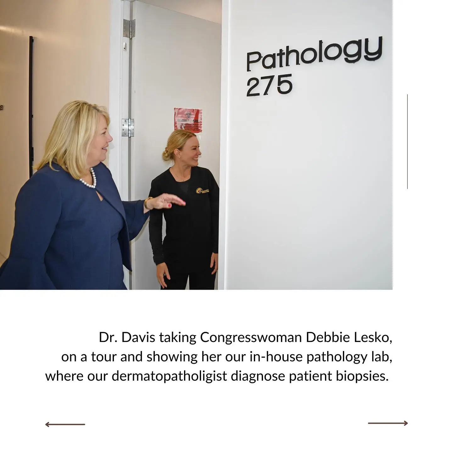 Two women standing outside a pathology lab door; one gestures while explaining the in-house facility where dermatopathologists diagnose patient biopsies